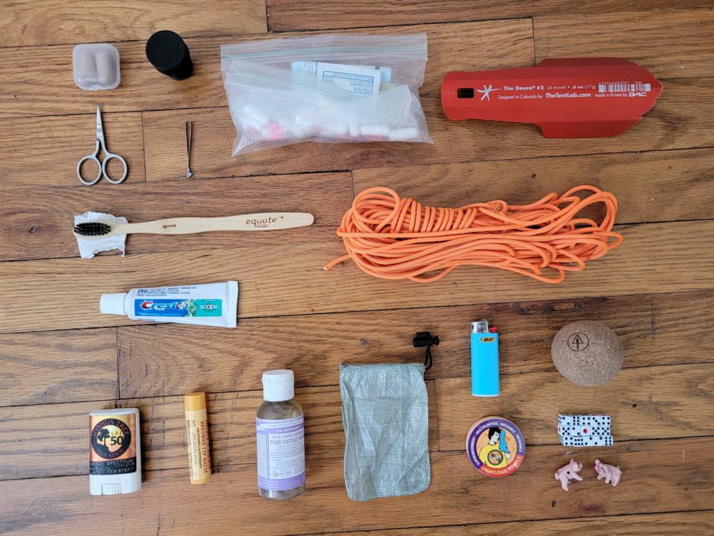 From left to right, top to bottom: foam earplugs, CuloClean bidet, first aid kit, Deuce of Spades #2, sewing scissors, tweezers, bamboo toothbrush, toothpaste, 50ft utility cord, Joshua Tree sun stick, Burt's Bees lip balm, Dr. Bronner's soap, wallet, Bic mini, Rawology cork ball, Lightload towel, mini dice, Pass the Pigs